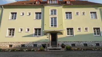 Vorderansicht eines gepflegten Mehrfamilienhauses mit hellgrüner Fassade und Steinsockel.