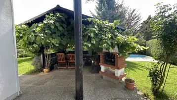 Gemütlicher überdachter Sitzbereich im Freien mit Grill und Blick auf den Pool im Garten.