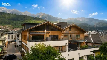 Moderne Holzfassade mit großen Fenstern und Bergblick unter strahlend blauem Himmel.
