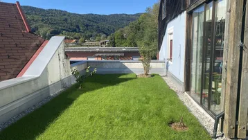 Grüner Rasenbereich mit Blick auf die umliegenden Berge und die Landschaft unter blauem Himmel.