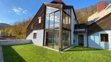 Modernes Haus mit großer Glasfassade und gepflegtem Rasenbereich im Garten unter blauem Himmel.