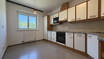Funktionale Küche mit Einbauschränken, Fliesenboden und Fenster mit Blick ins Grüne.
