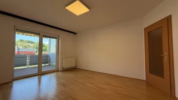 Helles, leeres Zimmer mit Parkettboden und Zugang zu einem Balkon, ideal als Wohn- oder Schlafzimmer.