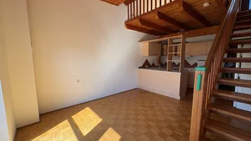 Heller Wohnbereich mit Holzdecke, Parkettboden und integrierter Küchenzeile unter einer Galerie.