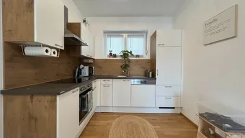 Moderne Küche mit weißen und holzfarbenen Schränken, integrierten Geräten und Fenster.
