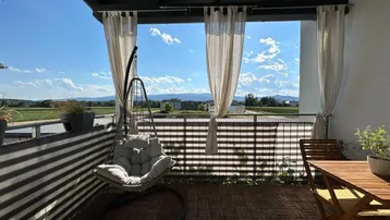 Geräumiger Balkon mit bequemer Hängeliege, Holzboden und weitem Blick ins Grüne.