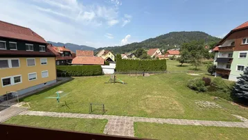 Weitläufiger Gemeinschaftsgarten mit Spielplatz und Blick auf die umliegende Berglandschaft.