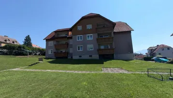 Mehrfamilienhaus mit mehreren Balkonen und gepflegter Rasenfläche in ländlicher Umgebung.