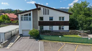 Ansicht des Hauses von vorne mit Parkplätzen und einem kleinen Gartenbereich.