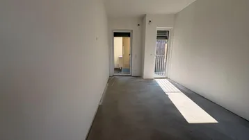Rohbau eines Schlafzimmers mit Betonboden, Zugang zu einem französischen Balkon und viel Tageslicht.