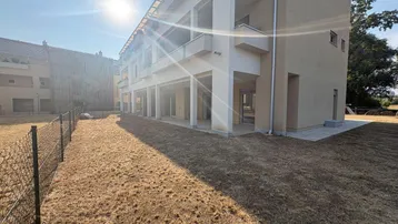 Außenansicht eines modernen Gebäudes mit großem, noch ungestaltetem Gartenbereich unter strahlendem Sonnenschein.