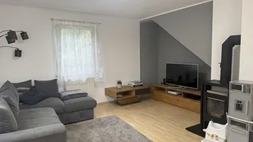 Wohnzimmer mit grauem Ecksofa, Holzofen und modernem TV-Möbel.