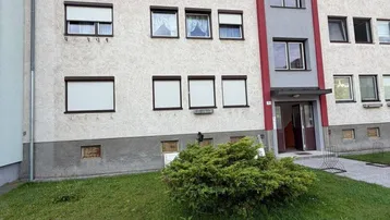 Mehrfamilienhaus mit weißer Fassade, roten Akzenten und gepflegtem Vorgartenbereich.
