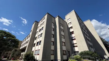 Modernes Mehrfamilienhaus mit markanter Betonfassade und roten Fensterrahmen unter blauem Himmel.