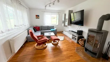 Gemütliches Wohnzimmer mit Holzboden, Ecksofa und einem modernen Holzofen.