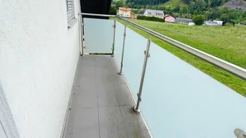 Moderner Balkon mit Glasgeländer und weitem Blick auf grüne Wiesen und Berge.