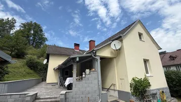 Seitenansicht des Hauses mit gepflasterter Terrasse, Treppenaufgang und Blick auf die grüne Umgebung.