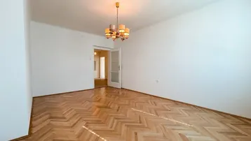 Helles Zimmer mit Fischgrätparkettboden, weißen Wänden und einem Kronleuchter, bereit zur Einrichtung.