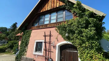 Rustikales Haus mit roter Fassade und üppigem Efeu bewachsen, unter blauem Himmel.