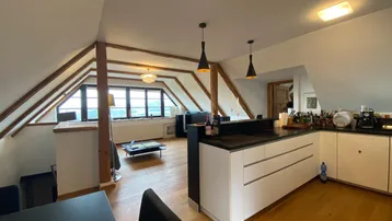 Offener Wohnbereich im Dachgeschoss mit Holzbalken, moderner Küche und weitem Ausblick.
