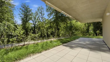 Grosse gepflasterte Terrasse mit Überdachung und Blick ins Grüne, ideal für Entspannung im Freien.