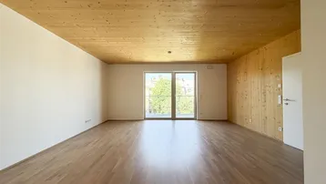 Heller, leerer Wohnraum mit Holzboden, Holzdecke und Zugang zu einem französischen Balkon.