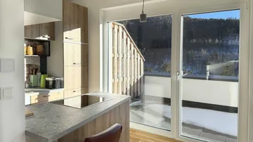 Moderne Küche mit Holzelementen, Steinplatte und Zugang zu einem Balkon mit Bergblick.