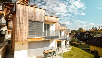Modernes Gebäude mit Holzfassade, Balkonen und Terrassen, umgeben von Grünflächen und Bäumen.