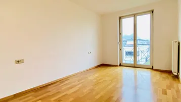 Helles Zimmer mit Parkettboden und Zugang zu einem französischen Balkon.
