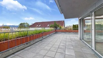 Große Dachterrasse mit Fliesenboden, Pflanzenkübeln und weitem Blick auf die Umgebung und Berge.