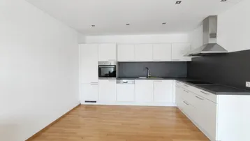 Moderne Einbauküche mit weißen Schränken, dunkler Arbeitsplatte und integrierten Geräten in einem hellen Raum.