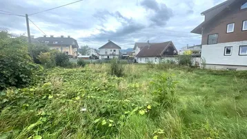 Blick auf ein unbebautes Grundstück mit umliegenden Wohnhäusern unter bewölktem Himmel.