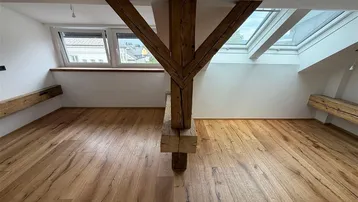 Heller Dachbodenraum mit sichtbaren Holzbalken, Holzboden und Dachfenstern, ideal für Wohnzwecke.