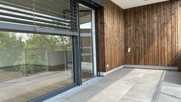 Geräumiger Balkon mit Fliesenboden, Holzverkleidung und Blick ins Grüne.