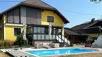 Gelbes Einfamilienhaus mit großem Garten, Pool und Sonnenterrasse unter blauem Himmel.