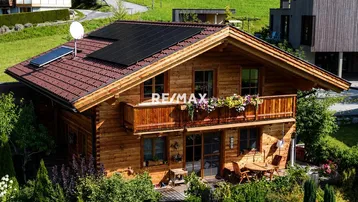 Charmantes Holzchalet mit Photovoltaikanlage, Balkon und gemütlichem Sitzbereich im Freien.