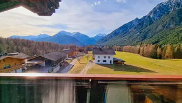 Blick vom Balkon auf die umliegende Berglandschaft und ein charmantes Haus im Tal.