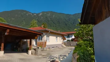 Blick auf das Haus mit Carport und der beeindruckenden Bergkulisse im Hintergrund unter blauem Himmel.