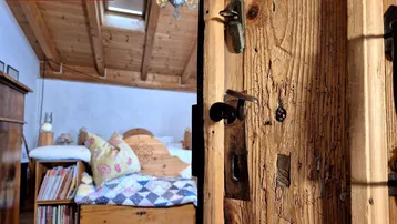 Rustikale Holztür öffnet sich zu einem gemütlichen Schlafzimmer mit Holzbalkendecke und Dachfenster.
