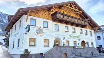 Traditionelles Gasthaus mit Holzbalkonen und bemalter Fassade vor einer Bergkulisse.