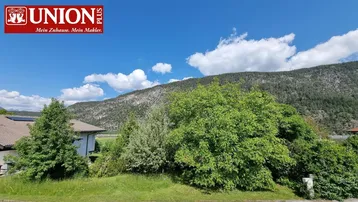 Panoramablick auf grüne Bäume und einen bewaldeten Berg unter einem strahlend blauen Himmel.
