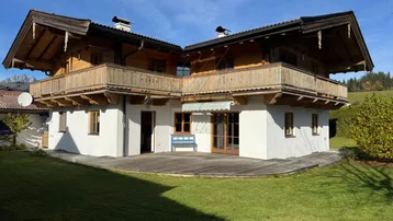 Traditionelles Holzhaus mit weißer Fassade, umlaufendem Balkon und großem Gartenbereich.