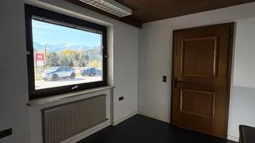 Heller Innenraum mit dunklem Boden, Holzdecke und Fenster mit Bergblick, ausgestattet mit einem Heizkörper.