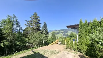 Gartenbereich mit Rasenfläche, Bäumen und weitem Blick auf die umliegende Berglandschaft unter blauem Himmel.