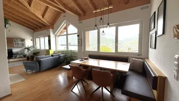 Helles Wohn- und Esszimmer mit Holzbalkendecke, Parkettboden und Bergblick durch große Fenster.