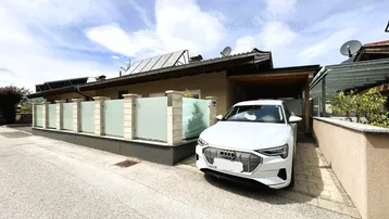 Außenansicht des Hauses mit Carport, Einfahrt und moderner Fassadengestaltung unter blauem Himmel.