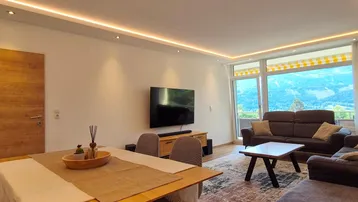 Helles Wohn- und Esszimmer mit Bergblick, modernen Möbeln und indirekter Deckenbeleuchtung.