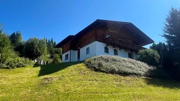 Traditionelles Chalet auf einem grünen Hügel mit Holzbalkonen und weitem Blick unter blauem Himmel.