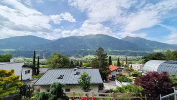 Weitläufiger Blick über die umliegende Landschaft mit Häusern, viel Grün und majestätischen Bergen.