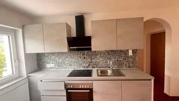 Moderne Einbauküche mit hellgrauen Fronten, Induktionskochfeld und Mosaikfliesen-Rückwand.